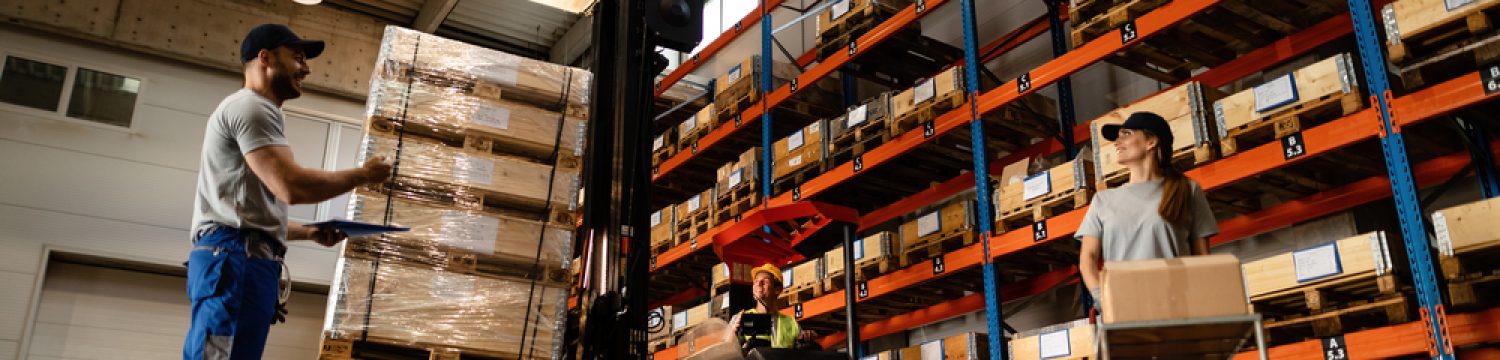 Low angle view of happy warehouse workers communicating while working with shipment in industrial storage compartment.